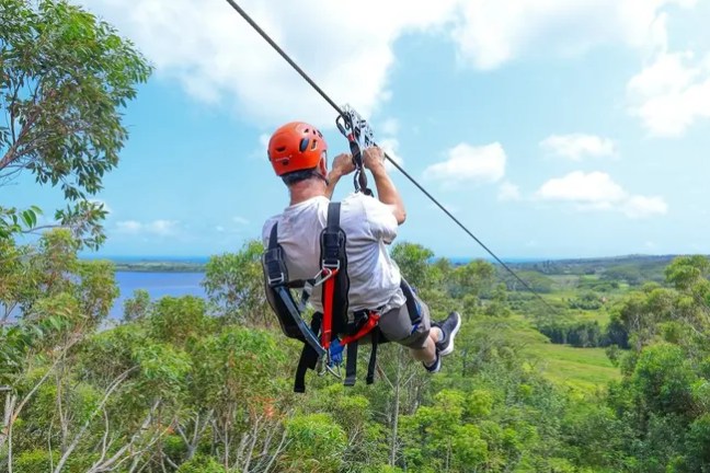 Person ziplining over lush green landscape with blue sky.