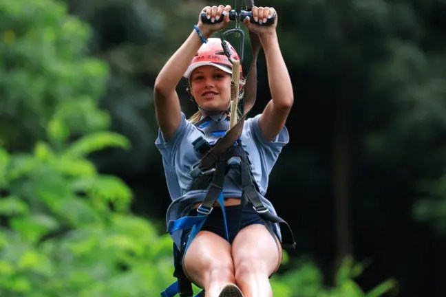 Person zip-lining in a forest wearing a helmet and harness.